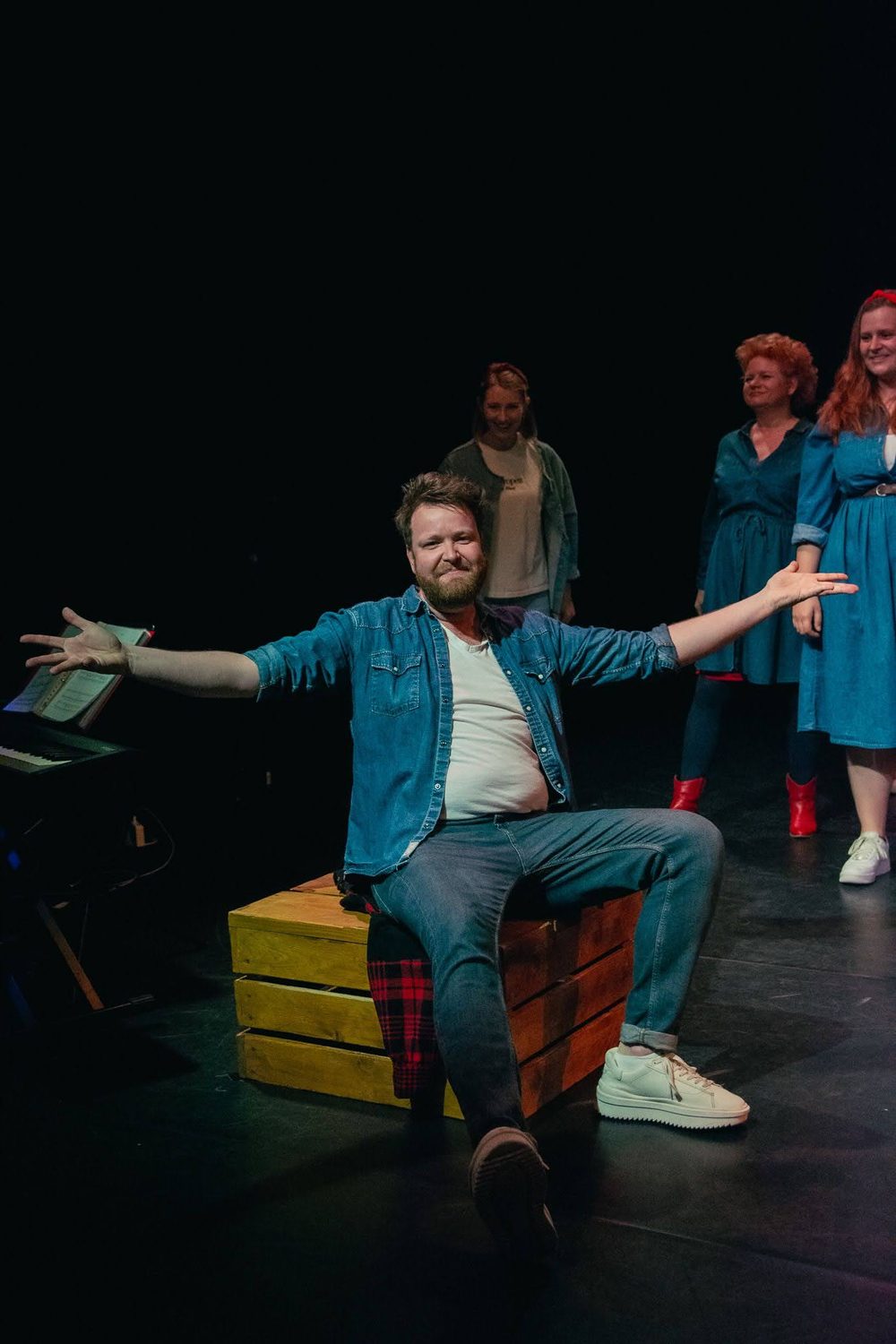 Jelle Gulmans zittend op een kist, zingend met gespreide armen, cast op de achtergrond